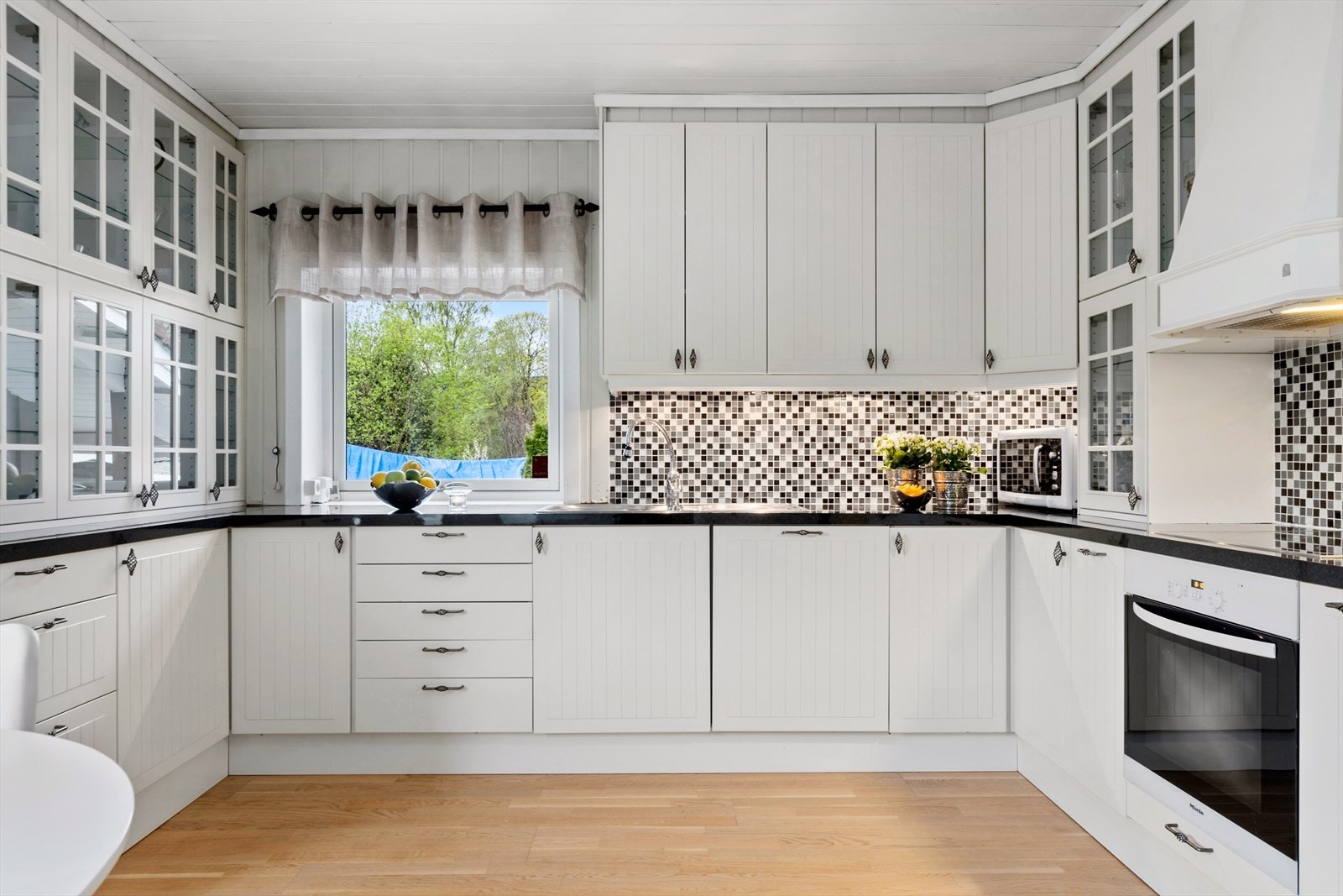 Velholdt og klassisk kjøkkeninnredning med hvite profilerte fronter og benkeplate av laminat. Galleribilde