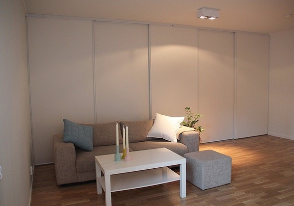 Stue har lyse forhold med 5 kvm stor skyvedørsgarderobe/ lagringsløsning bak sofa. Galleribilde