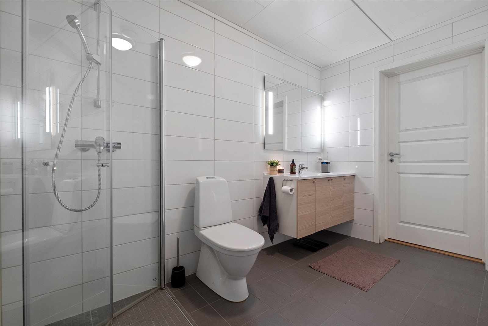 Bad med fliser og varmekabler i gulv, flis på vegger. Dusjhjørne med glassdører, toalett, hel servantplate med underskap, fordelerskap for vann, opplegg for vaskemaskin, vv-bereder, stoppekran. Ventilasjon i himling. Galleribilde