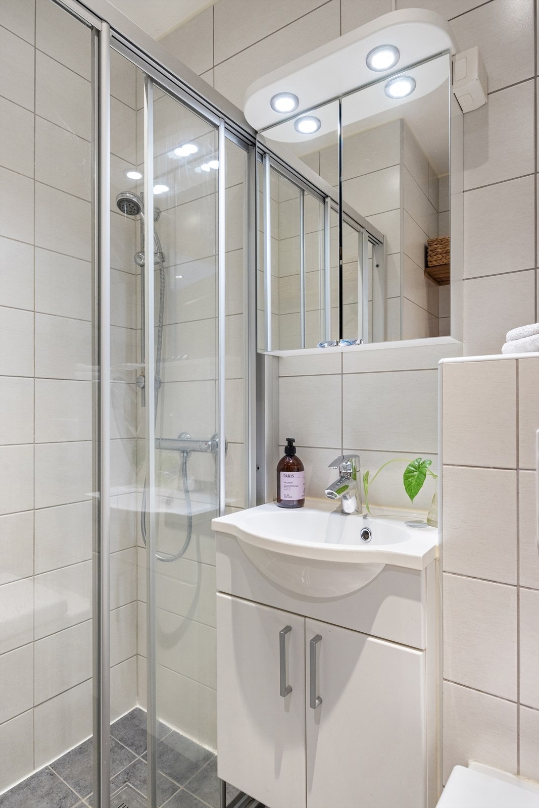 Badet er innredet med vegghengt klosett, servant med innredning, speil med lys og dusjhjørne med skyvbar glassdør. Galleribilde