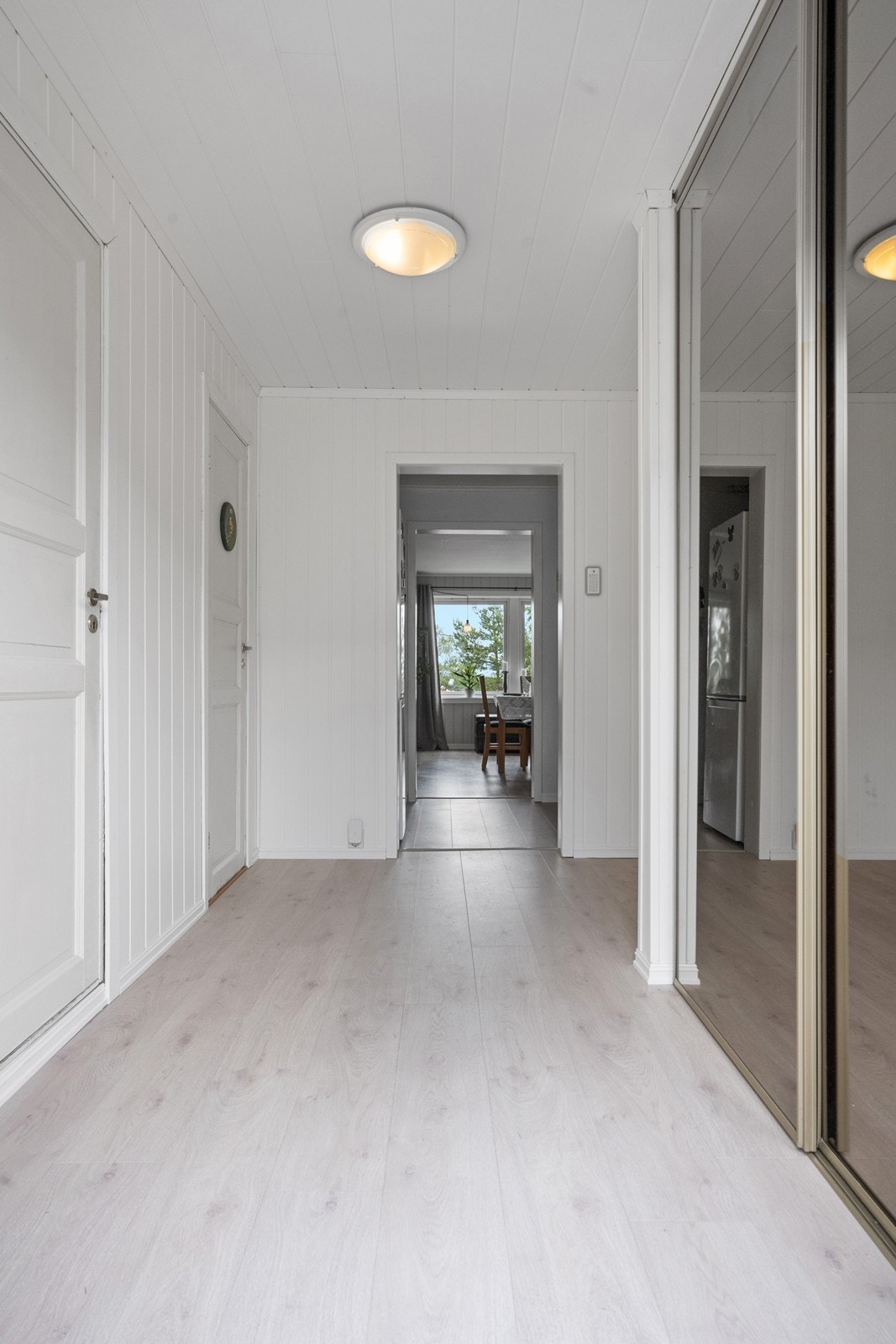 Lys og pen gang/entré med moderne en-stavs laminat på gulvet. Her er det montert en praktisk skyvedørsgarderobe med speilfronter Galleribilde