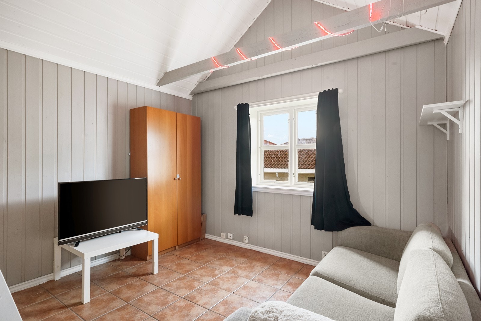Stue/oppholdsrom i annekset med fliser på gulvet og malt panel på vegger og i himling Galleribilde