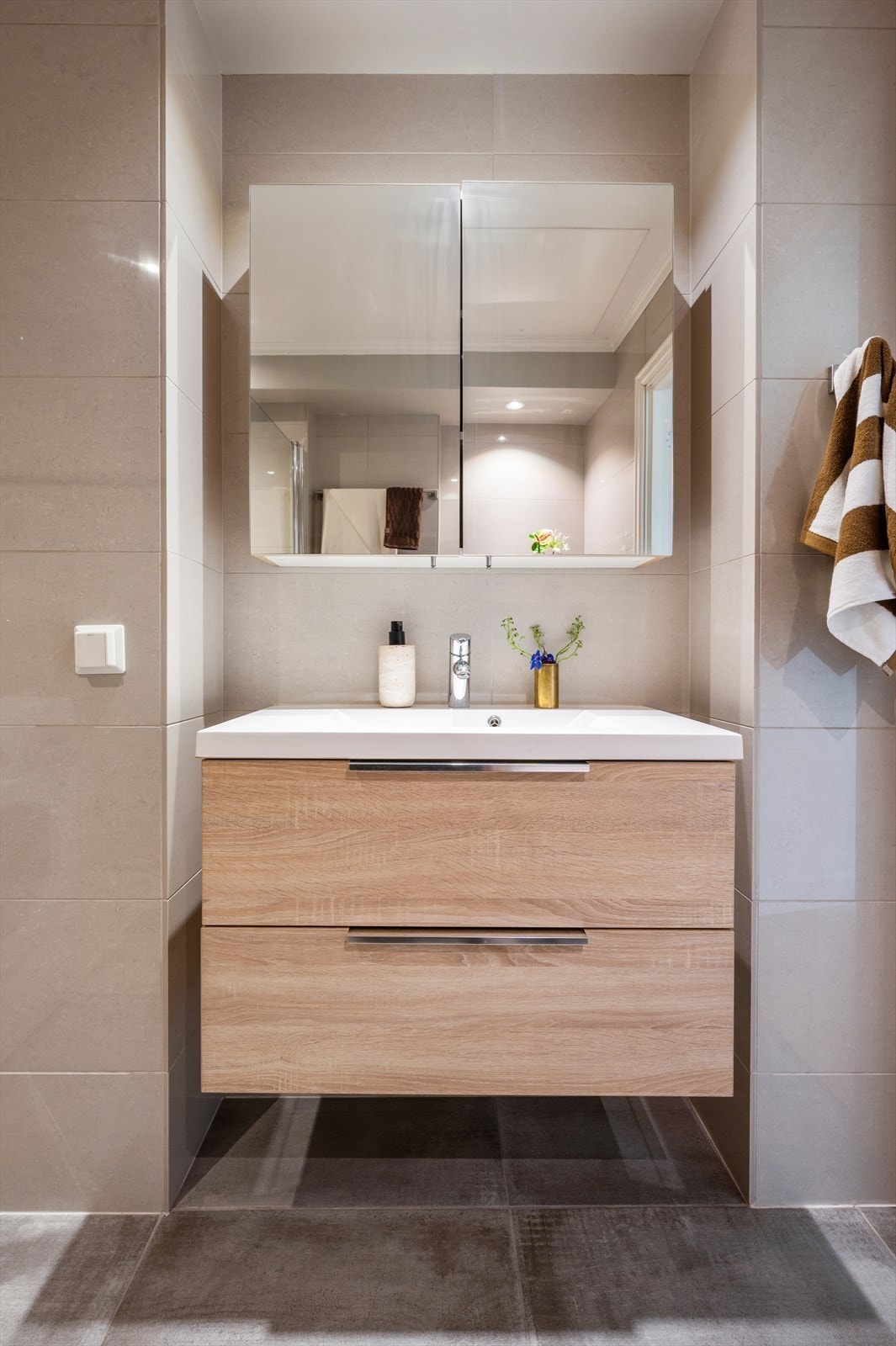 Stilrent innredet med fliser på både gulv og vegger, samt malte plater i himlingen med innfelt downlights. Badet er utstyrt med vegghengt toalett, servant nedfelt i innredning, speilskap og dusjhjørne med svingbare glassdører. Galleribilde