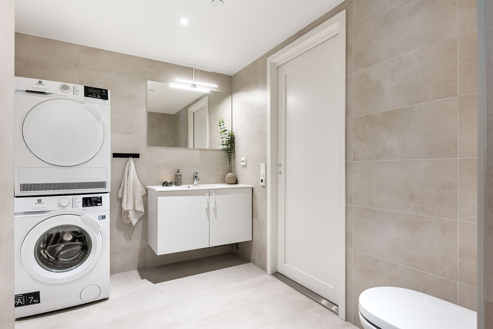 Stilig baderom med nedfelt servant, vegghengt toalett, dusj og opplegg for vaskemaskin. Galleribilde