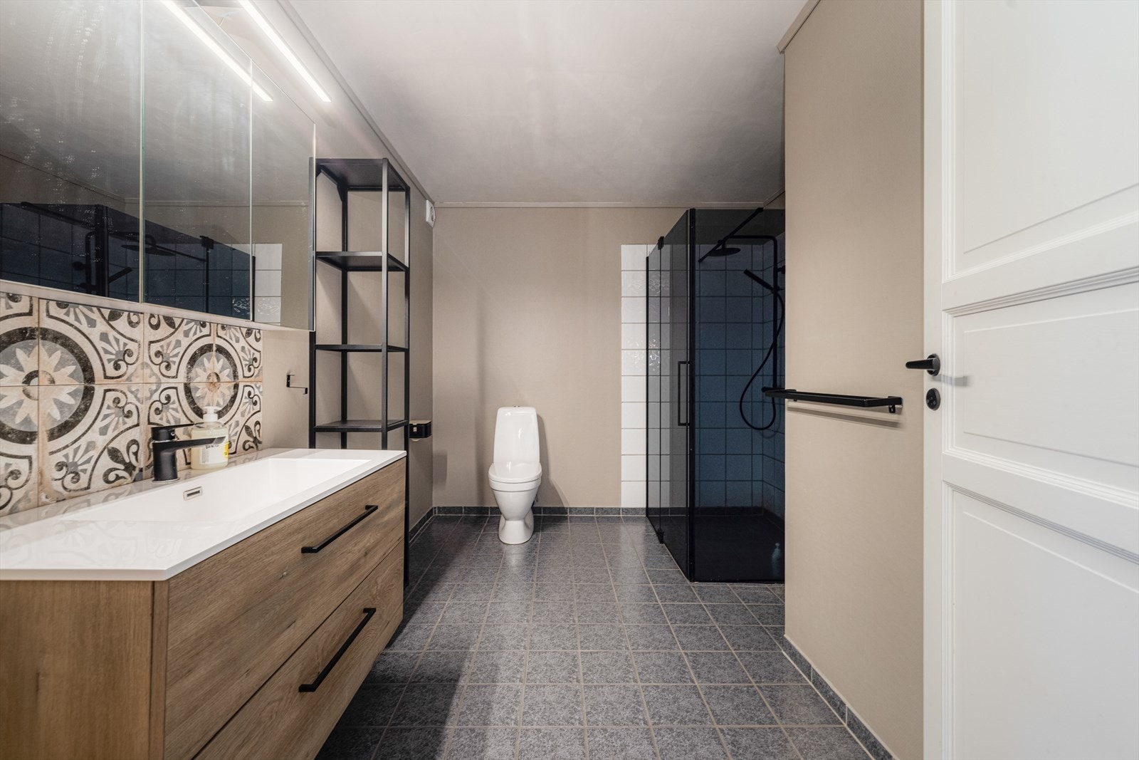 Innbydende baderom fra byggeår hvor baderomsinnredning og dusjdører er nye fra 2021. Flislagt gulv med gulvvarme, malte vegger med flis på vegg i dusjsone. Innredningen med heldekkende servantplate i pent utseende, speilskap med belysning over vask. Galleribilde