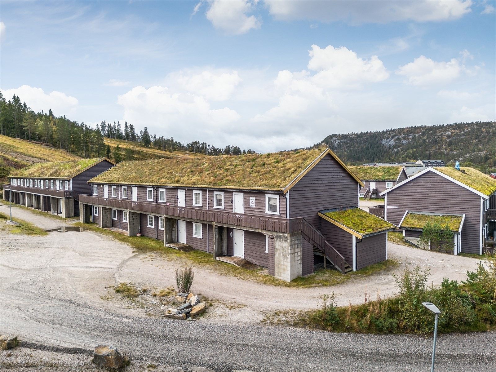 Tomten er opparbeidet med gruset innkjørsel og stor gårdsplass. Det er kjørevei frem til inngangsdøra for av- og pålessing, hvor denne leiligheten ligger lettvint til i 1. etasje i den ene enden av bygget. Galleribilde