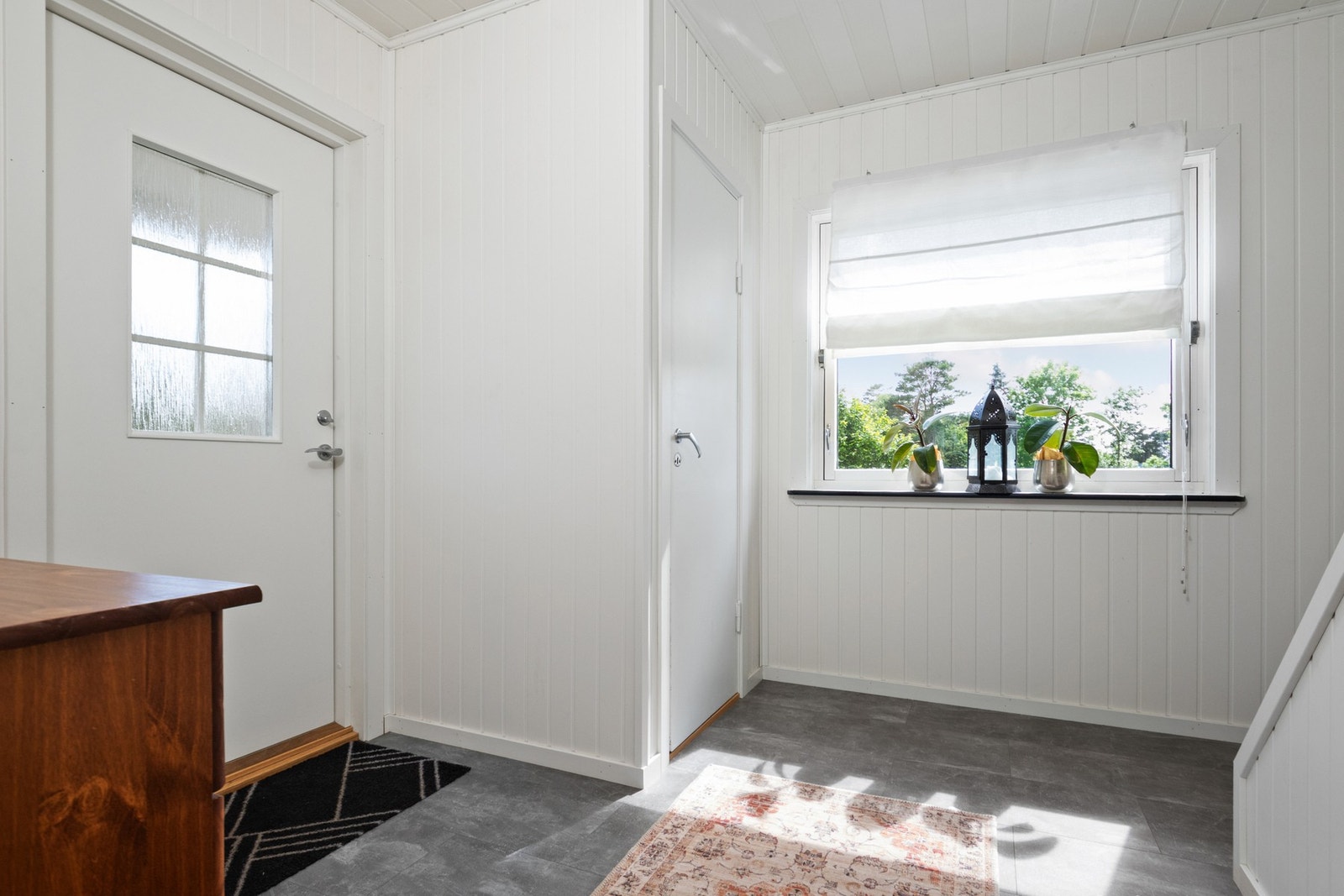 Lys og fin entré med hvitmalt panel på veggene og grått flislaminat på gulvet. Galleribilde
