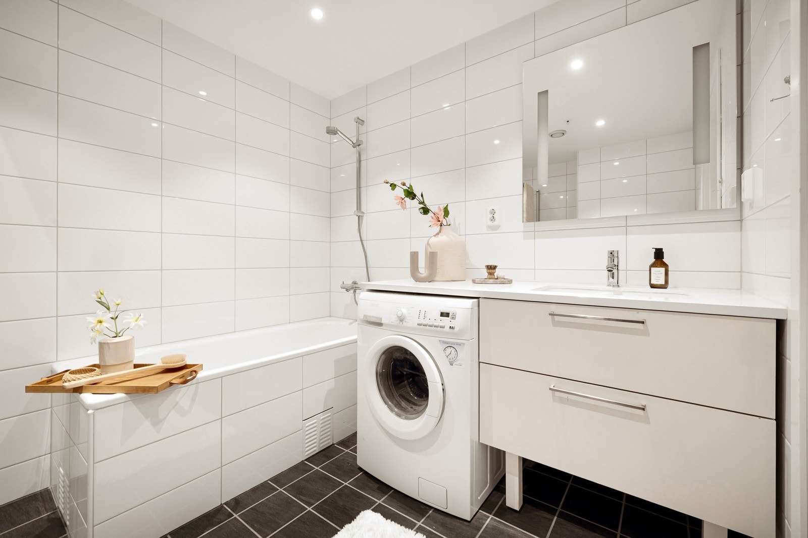 - Badet er delikat innredet med fliser på gulv og vegger, badekar, dusj med foldedører, vegghengt toalett og servant med møblement - Galleribilde