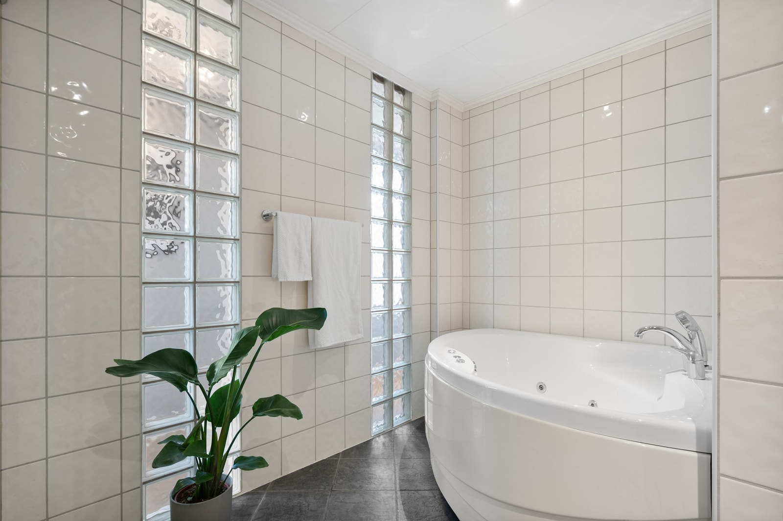 Delikat hjørnebadekar og stilfull bruk av glassbyggerstein som slipper inn lys og gir en luftig romfølelse. Galleribilde