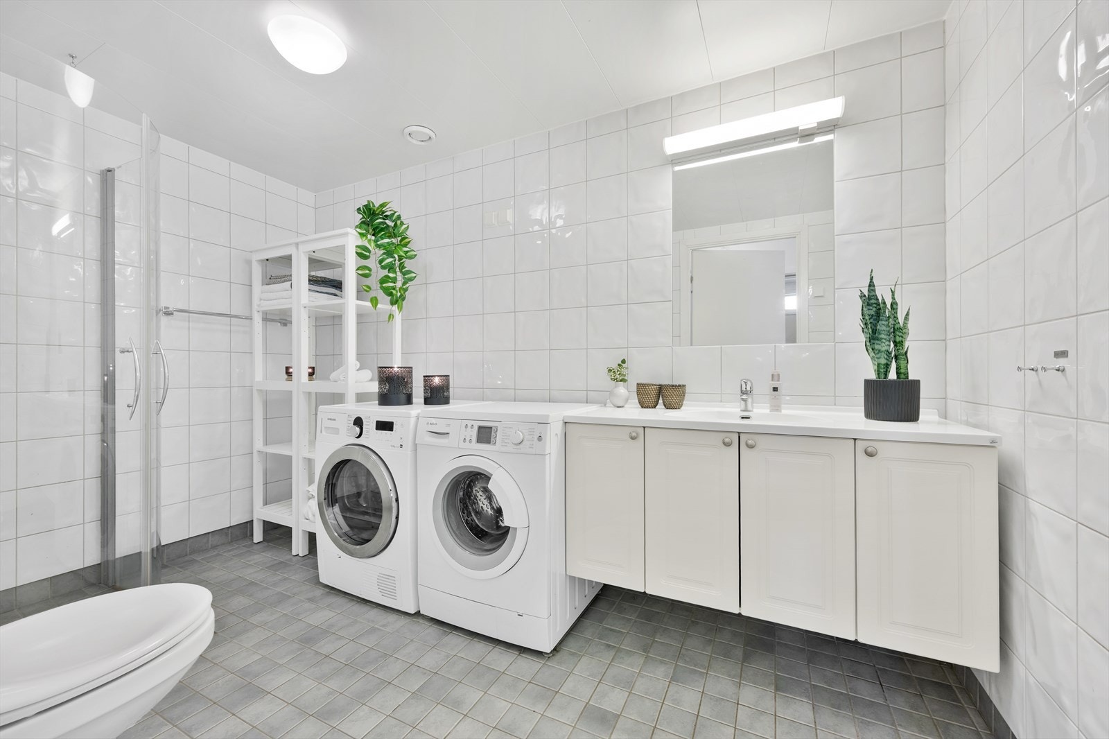 Badet er innredet med servant i baderomsinnredning, speil med belysning over, toalett, dusjhjørne og opplegg for vaskemaskin. Galleribilde