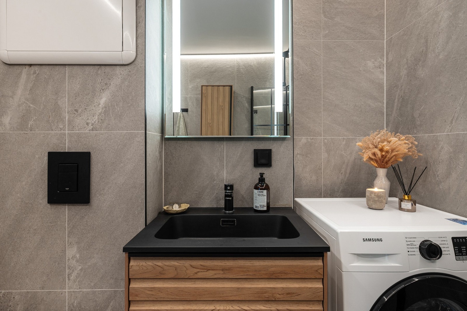 Moderne innredning med ovenpåliggende servant, speil med lys og stikkontakt. Det er opplegg for vaskemaskin på badet. Galleribilde