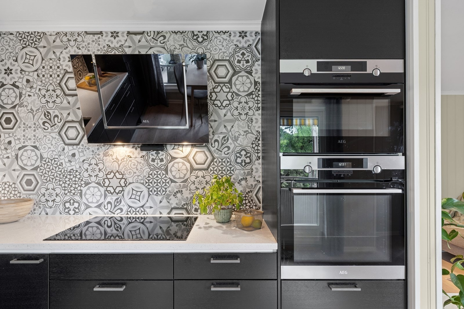 Innredning med sorte fronter, fliser over benkeplate i stein, oppvaskkum, kjøkkenventilator med kullfilter, opphøyd komfyr og mikro, induksjonstopp, oppvaskmaskin og kjøl-/fryseskap. Galleribilde