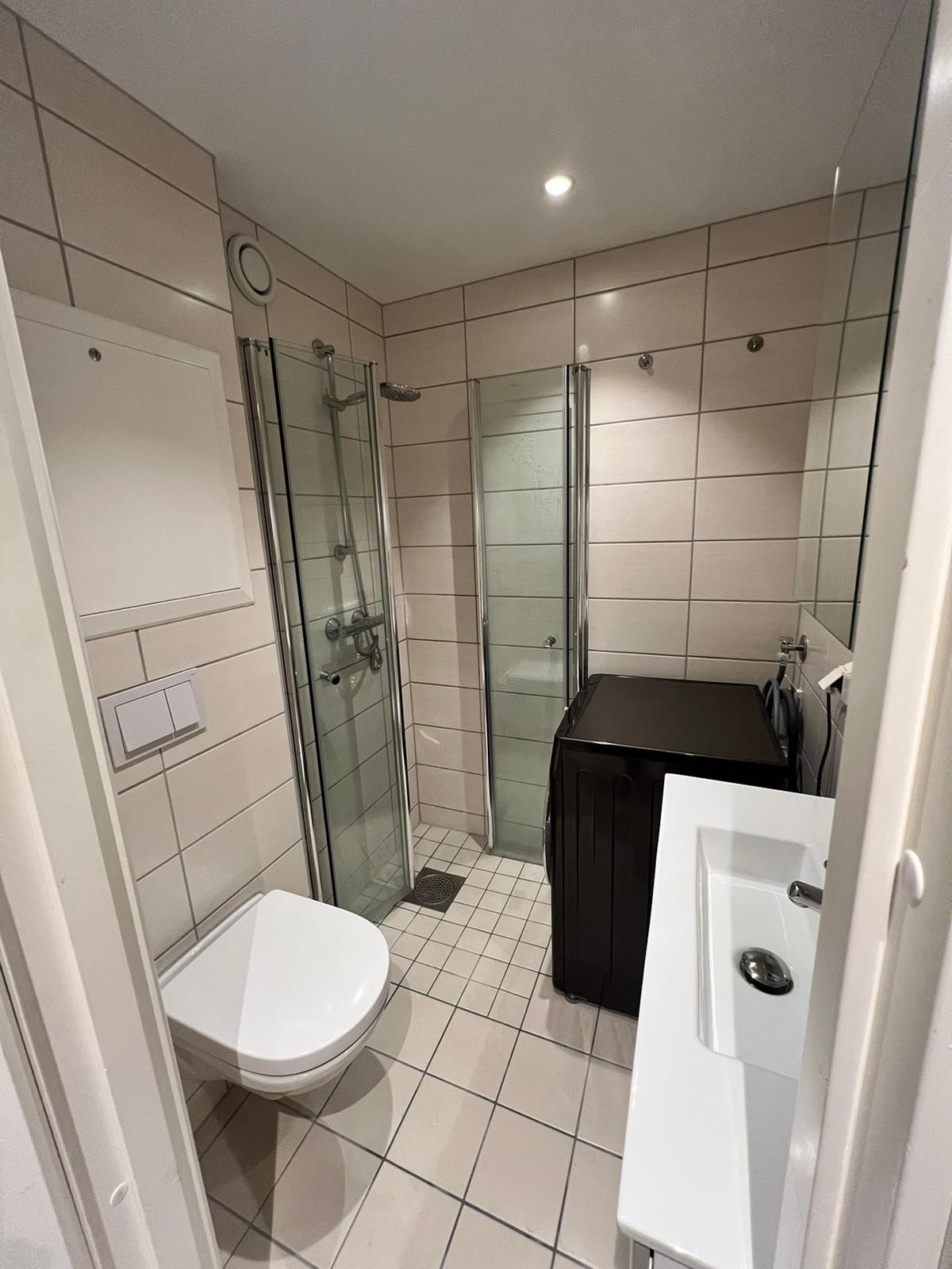 Komplett flislagt bad med varme i gulvet, dusjhjørne, vaskemaskin, servant og toalett. Galleribilde