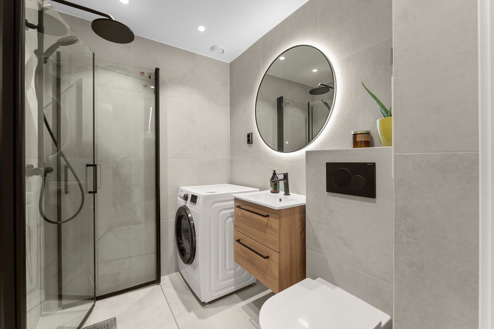 Badet er nytt fra 2025 og har ikke vært i bruk. Gulv og vegger er flislagte, og det er vannbåren gulvvarme. Baderomsinnredningen består av glatte, folierte fronter med heldekkende servant, speil med lysarmatur, vegghengt toalett og dusjhjørne med rette gl Galleribilde