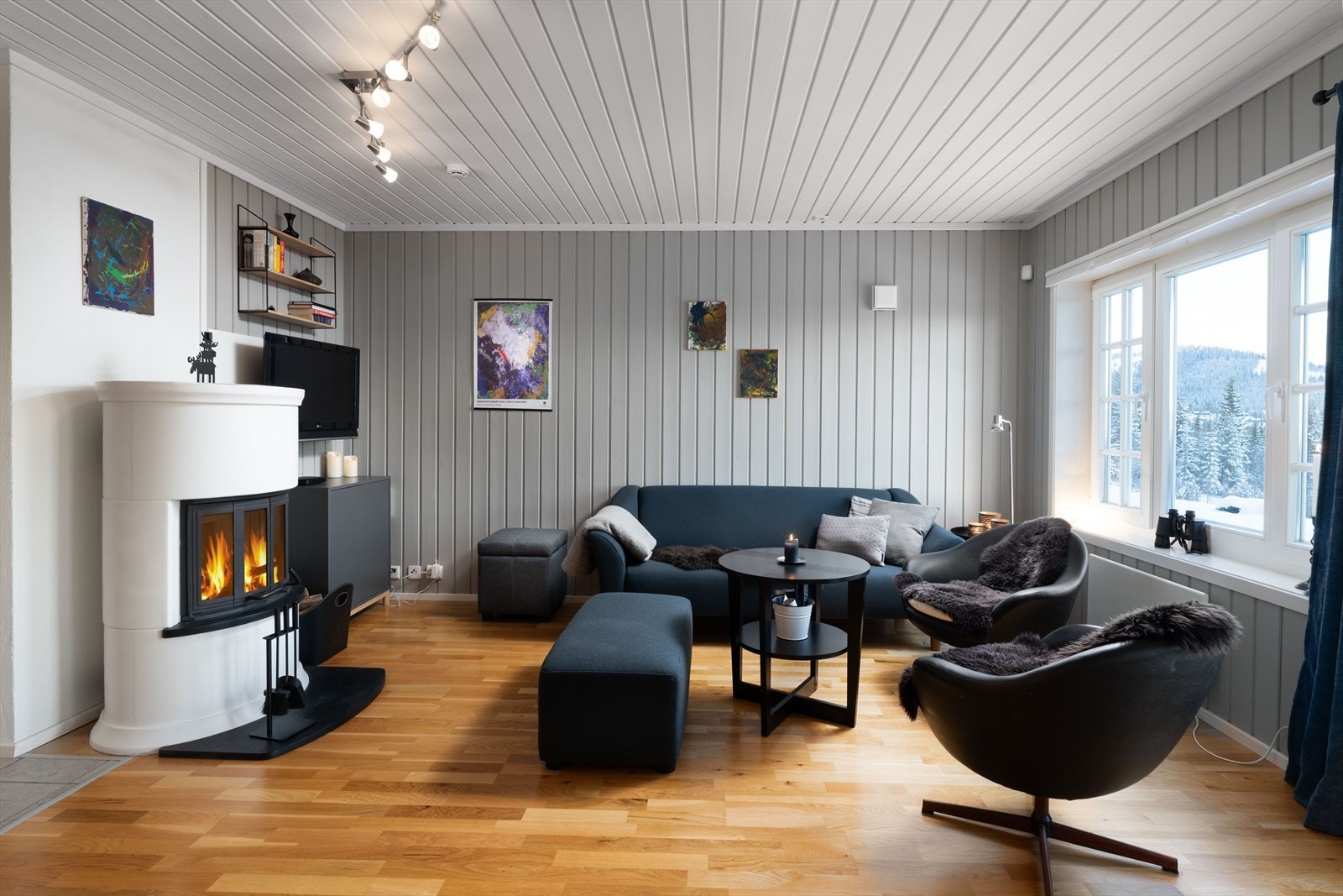 Panelte overflater malt i tidløs farge, og parkett på gulv. Peisovnen gir kos og god varme i den kalde årstida. Galleribilde