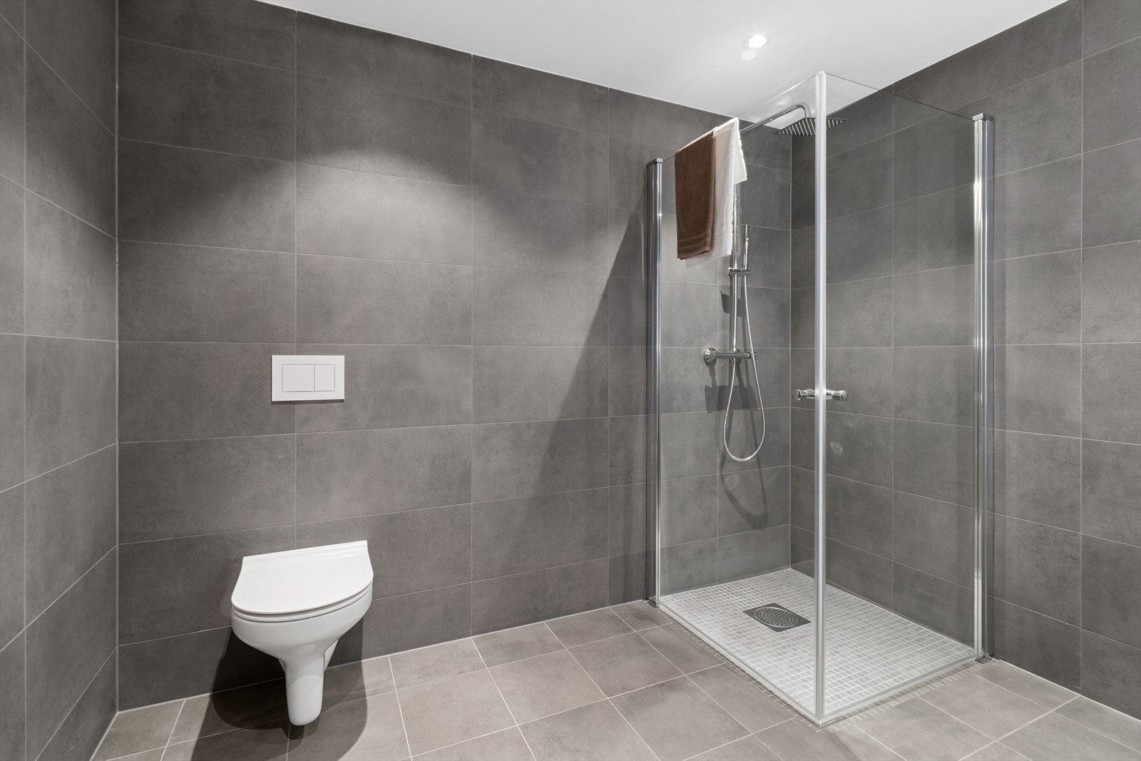 Badet er bestående av vegghengt toalett med soft close sete og en romslig dusj med rainfall dusj, samt armatur i krom. Galleribilde