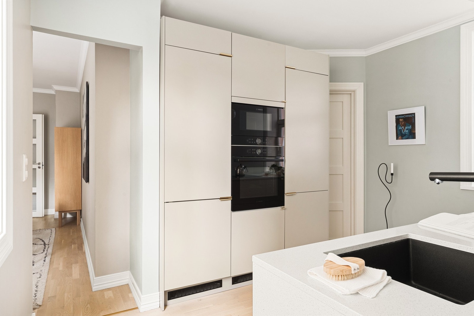 Kjøkkeninnredningen har moderne, slette fronter i en elegant fargetone, kombinert med en eksklusiv benkeplate i stein som gir et tidløst uttrykk. Galleribilde