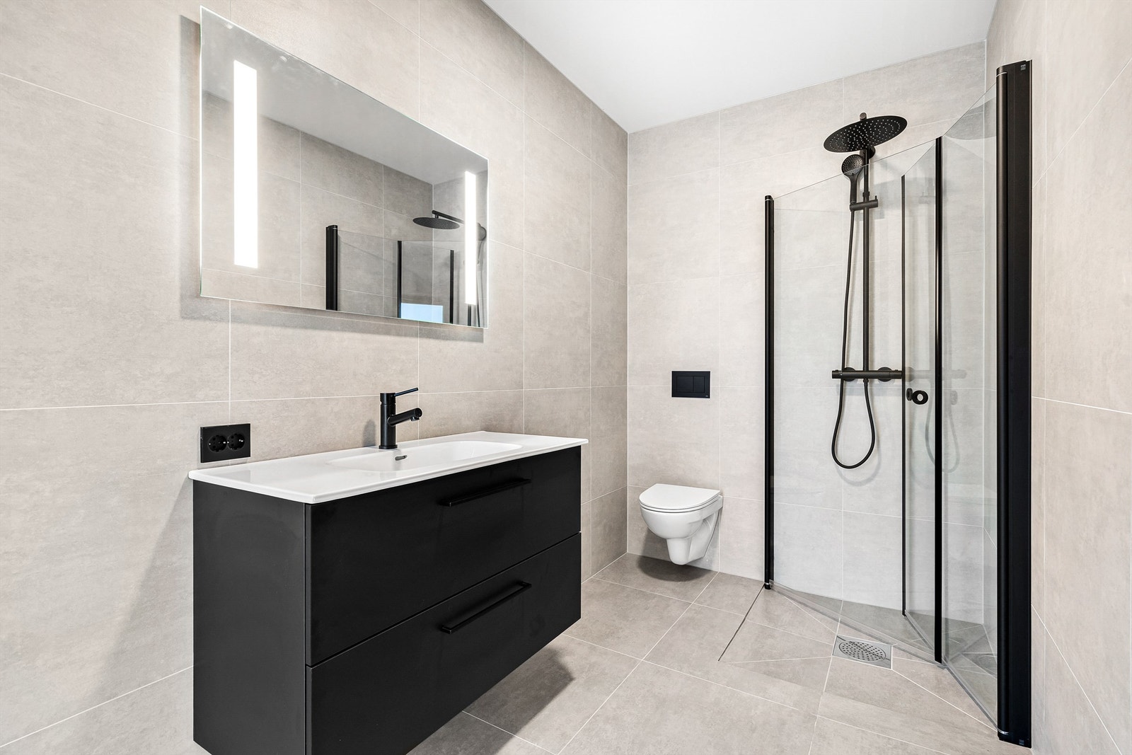 Lekkert flislagt bad med dusjnisje og regndusj, vegghengt toalett, servant med innredning samt speil med lys. Galleribilde