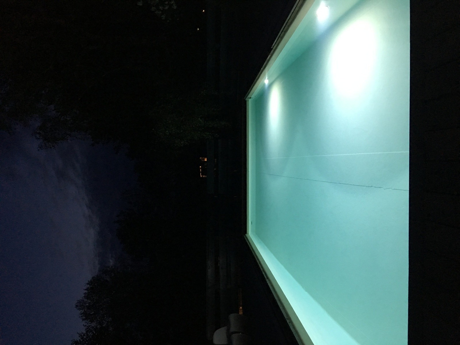 Opplyst svømmebasseng i mørket med trær i bakgrunnen. Galleribilde