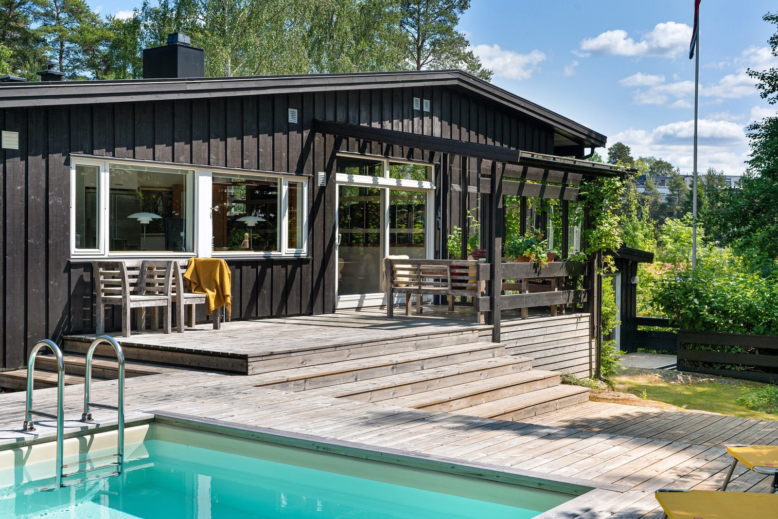 Moderne bolig med stor terrasse og svømmebasseng, omringet av frodig natur. Store vinduer gir mye naturlig lys. Galleribilde