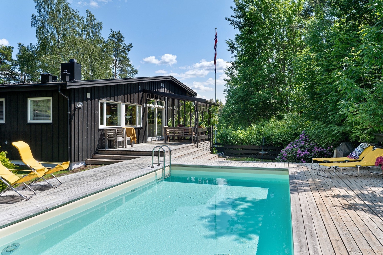 Boligen har en stor terrasse med svømmebasseng og sittegruppe, omgitt av frodige trær og busker. Galleribilde