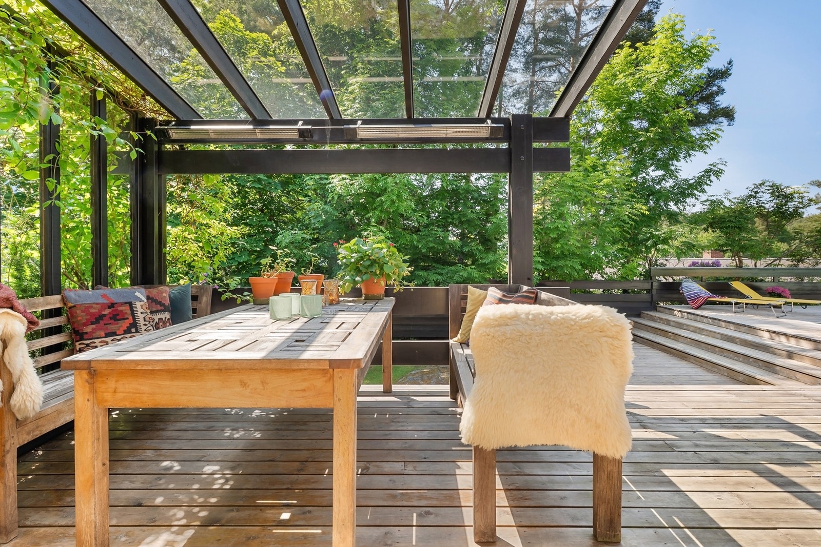 Overbygget terrasse med spisebord, benk og stoler, omgitt av grønn vegetasjon. Galleribilde