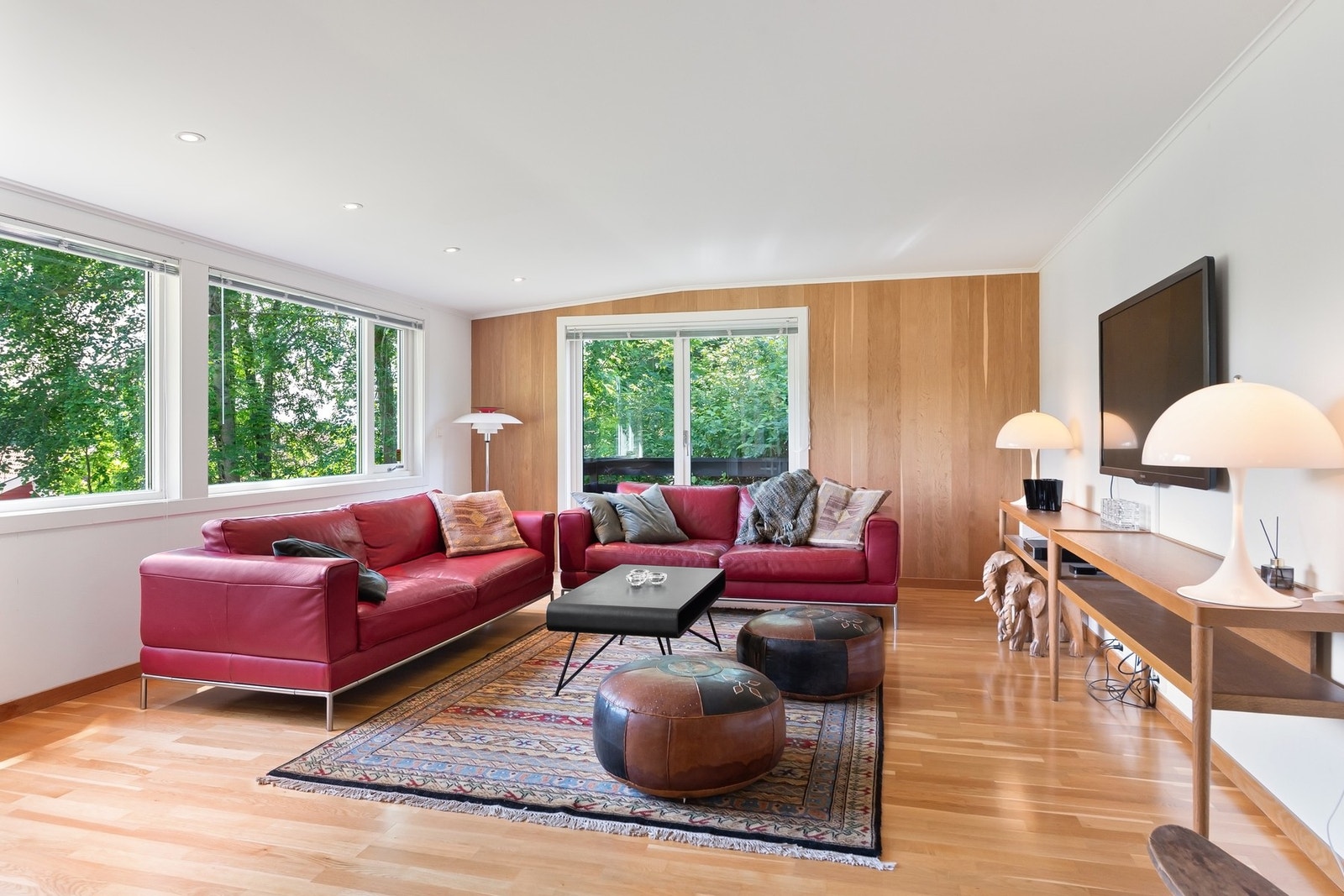 Lyst oppholdsrom med store vinduer, tregulv og en trevegg. Galleribilde