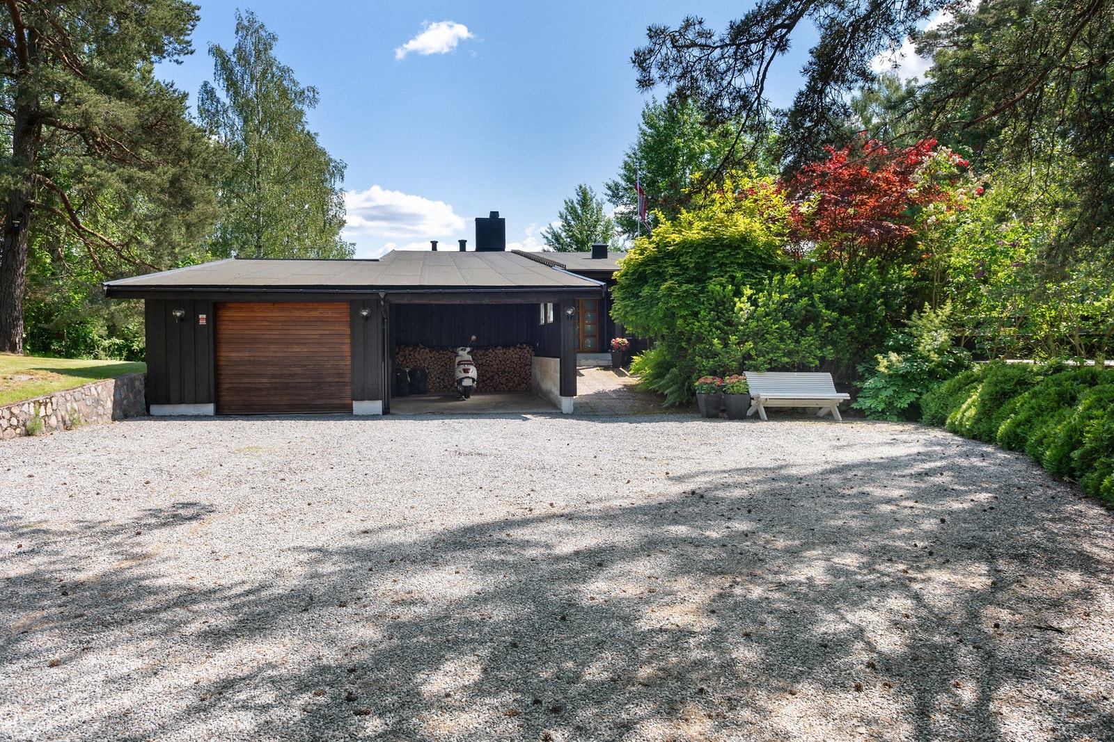 Enebolig med stor gruslagt gårdsplass, integrert garasje og frodig beplantning rundt. 2011. Spesialbestilt garrasjeport/boddører i varmebehandlet ask innstallert. (Bygg-It) Galleribilde