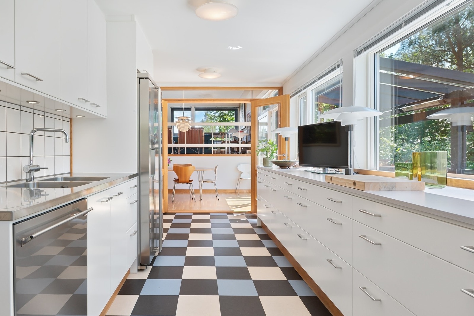 Lyst og moderne kjøkken med sjakkrutete gulv, store vinduer og åpen løsning mot spisestue. Galleribilde