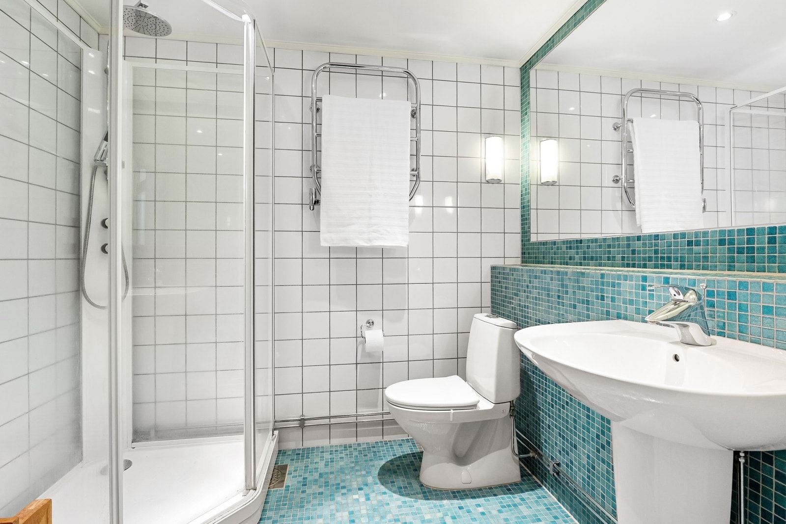 Lyst bad med dusjkabinett, toalett og servant. Vegger og gulv er flislagt. Galleribilde