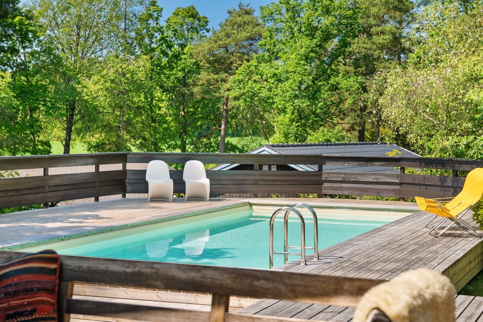 Uteområde med svømmebasseng, treterrasse og sitteplasser omgitt av frodig vegetasjon. Galleribilde