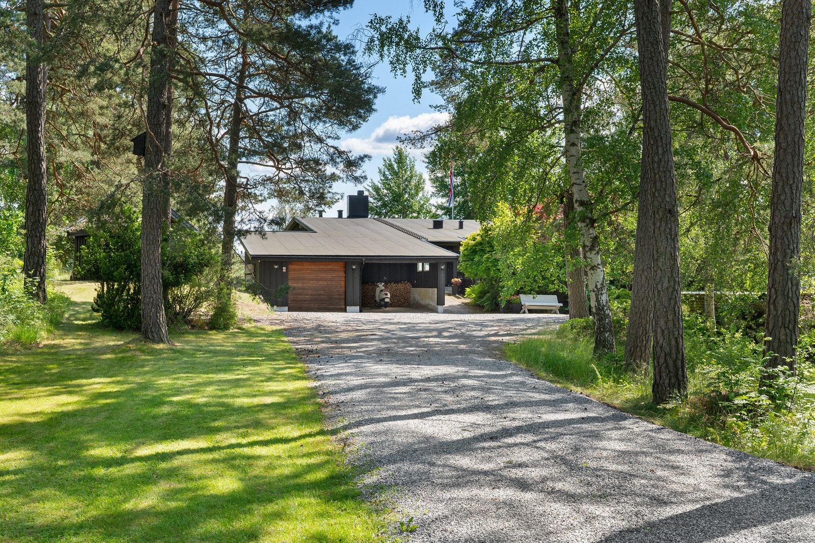 Grusvei leder til enebolig omgitt av trær og grøntområder. Eiet tomt på over 2,4 mål. Galleribilde