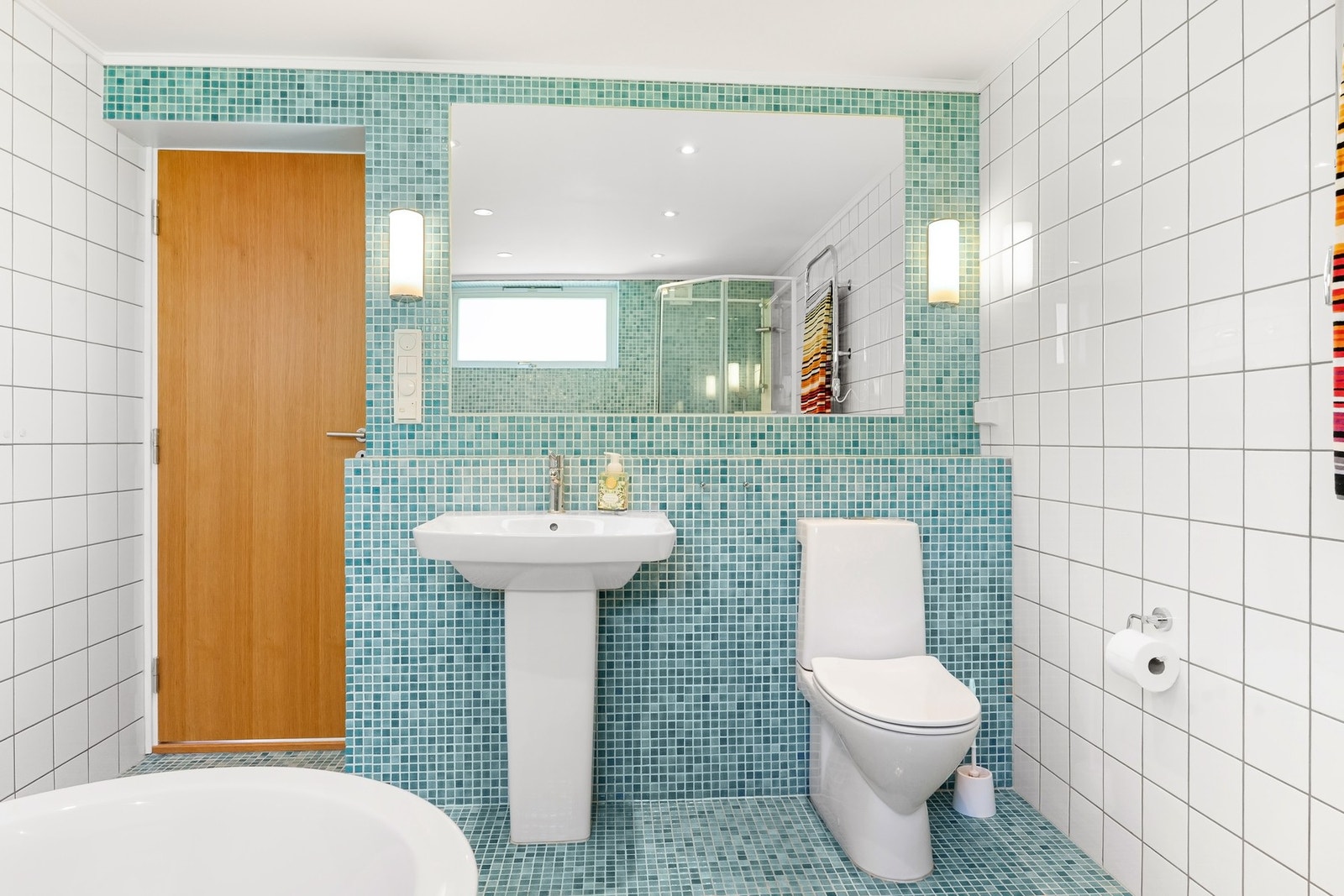 Badet har hvite og turkise fliser, toalett, servant og stort speil med belysning. 2010 ble badt nede. Varmekabler, fliser, vindu. (Bygg-It, Kolås, O Hansens eftf, Rolf Andreassen og sønner) Galleribilde