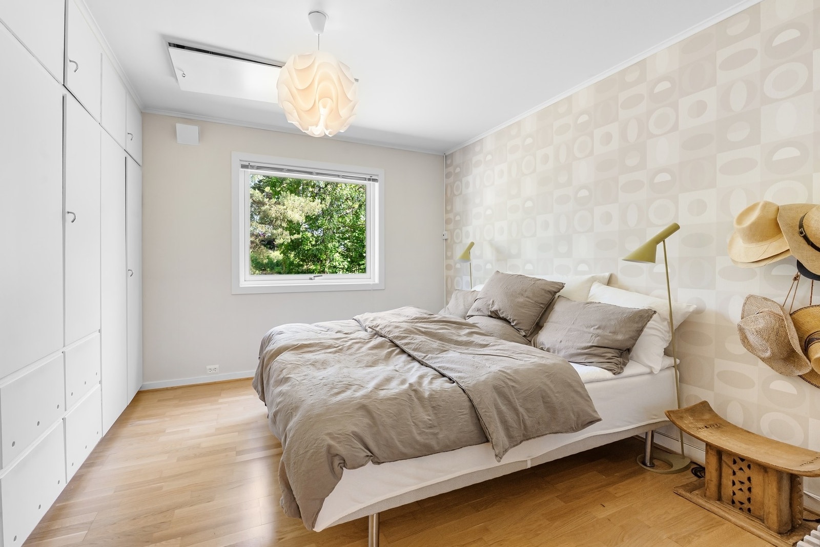 Soverom med stor seng, vindu mot grøntområde, hvite skap og tregulv. Galleribilde