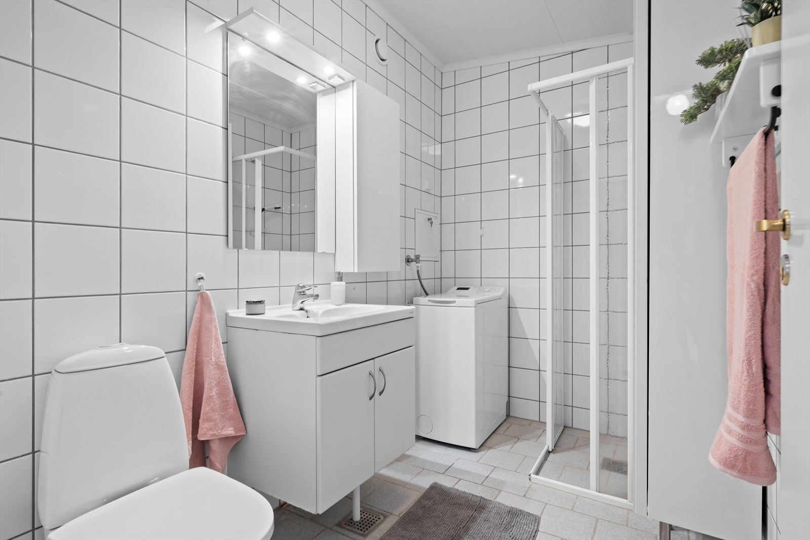 Badet er utstyrt med wc, innredning med underskap og et overskap. veggheng speil med belysning, dusjhjørne, avtrekksventil og opplegg for vaskemaskin. Galleribilde