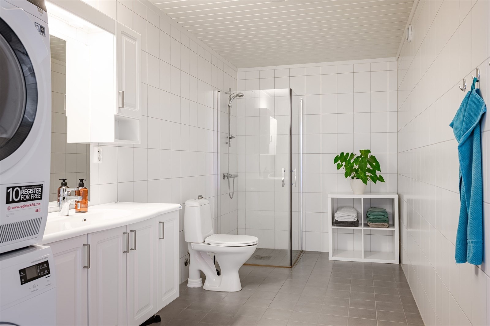 Baderommet er også utstyrt med dusjhjørne med innfellbare glassdører og gulvstående toalett. I hjørnet er det plass og opplegg for vaskemaskin og tørketrommel over om ønskelig. Galleribilde