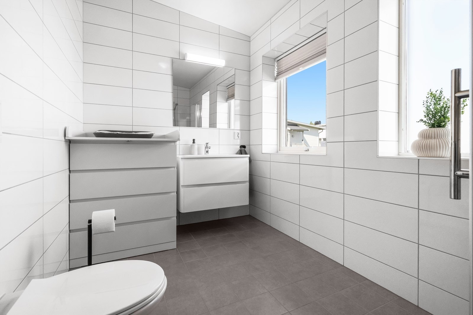 Rommet er innredet med servantinnredning med slette, lyse fronter og overhengende speil med belysning. Galleribilde