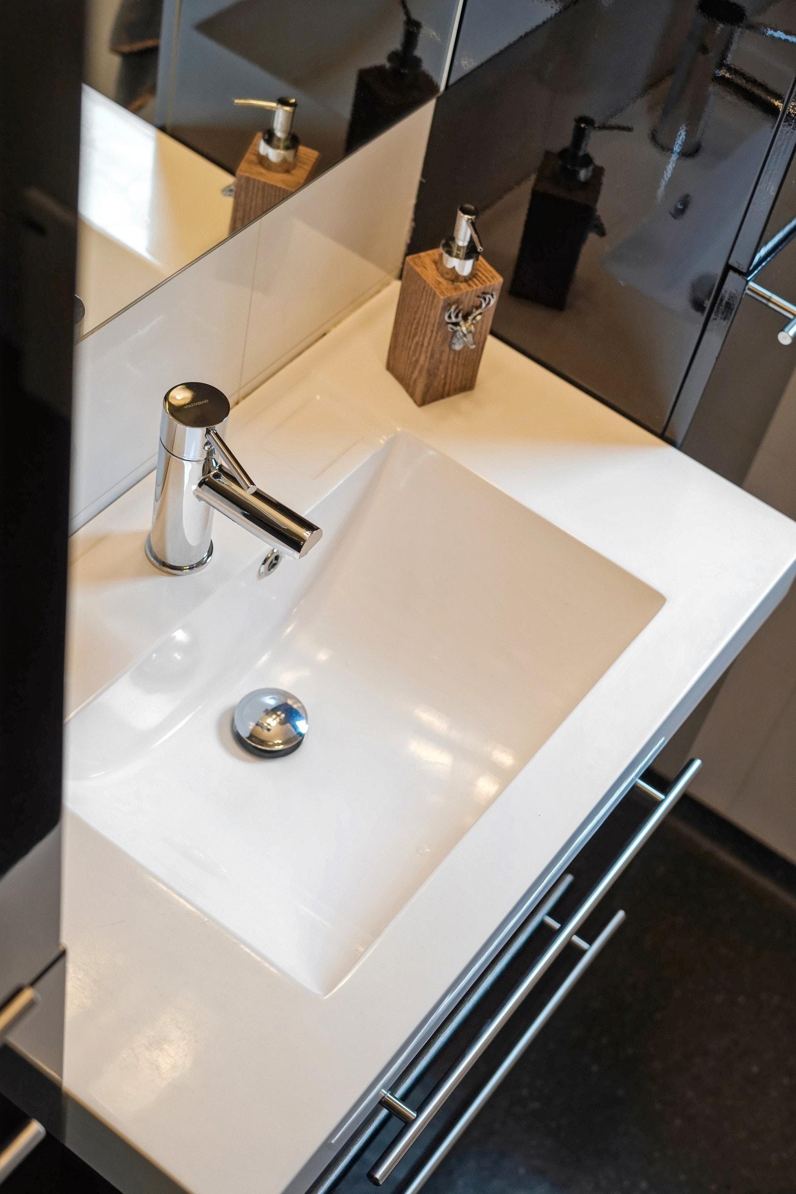 Innredning med mørke fronter i høyglans og hvit helstøpt servant. Speil med belysning over. Galleribilde