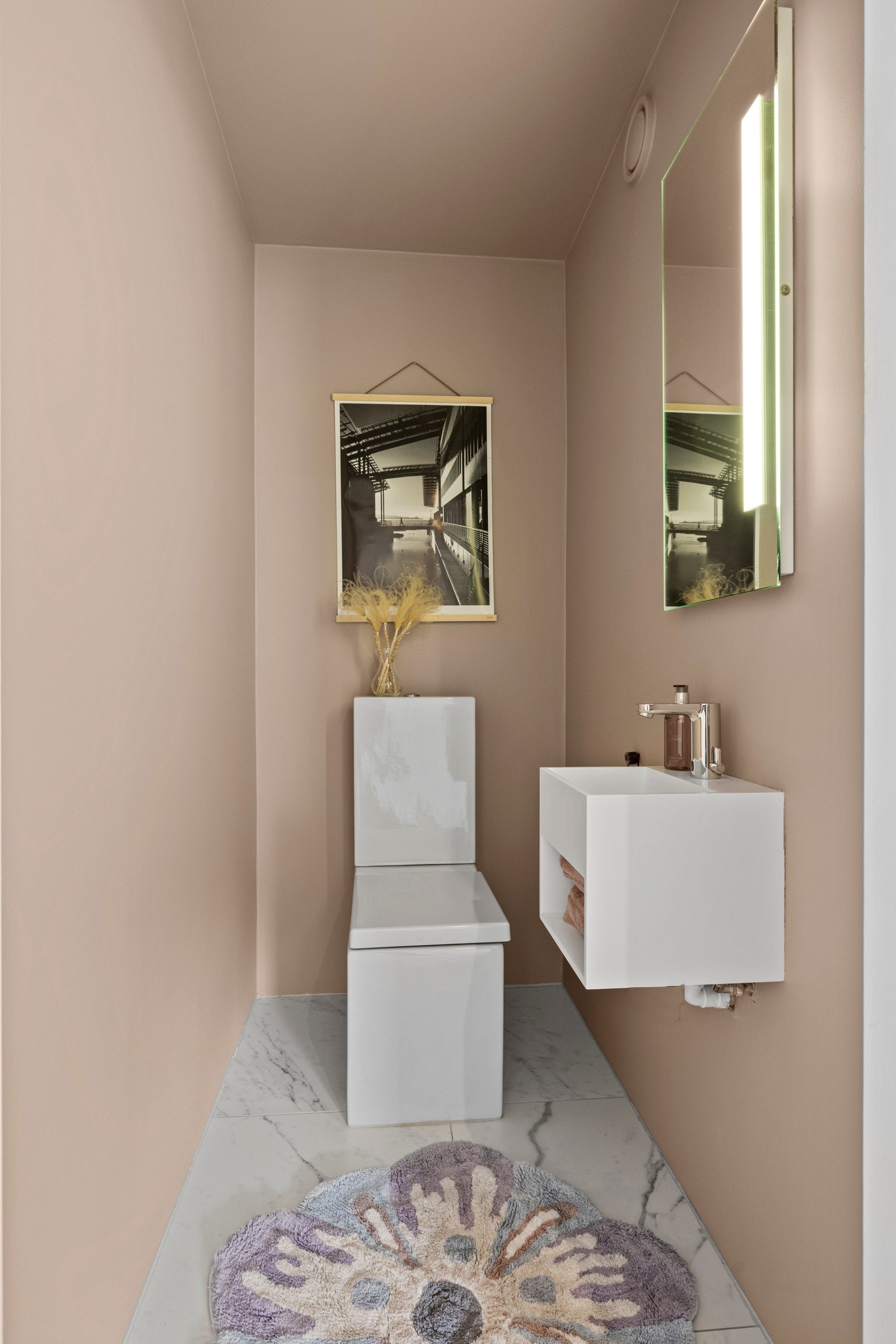 Toalettrommet er flislagt, har varmekabler i gulvet og er utstyrt med et toalett og en elegant Corian-servant. Dette rommet er perfekt for både større husholdninger og gjester Galleribilde