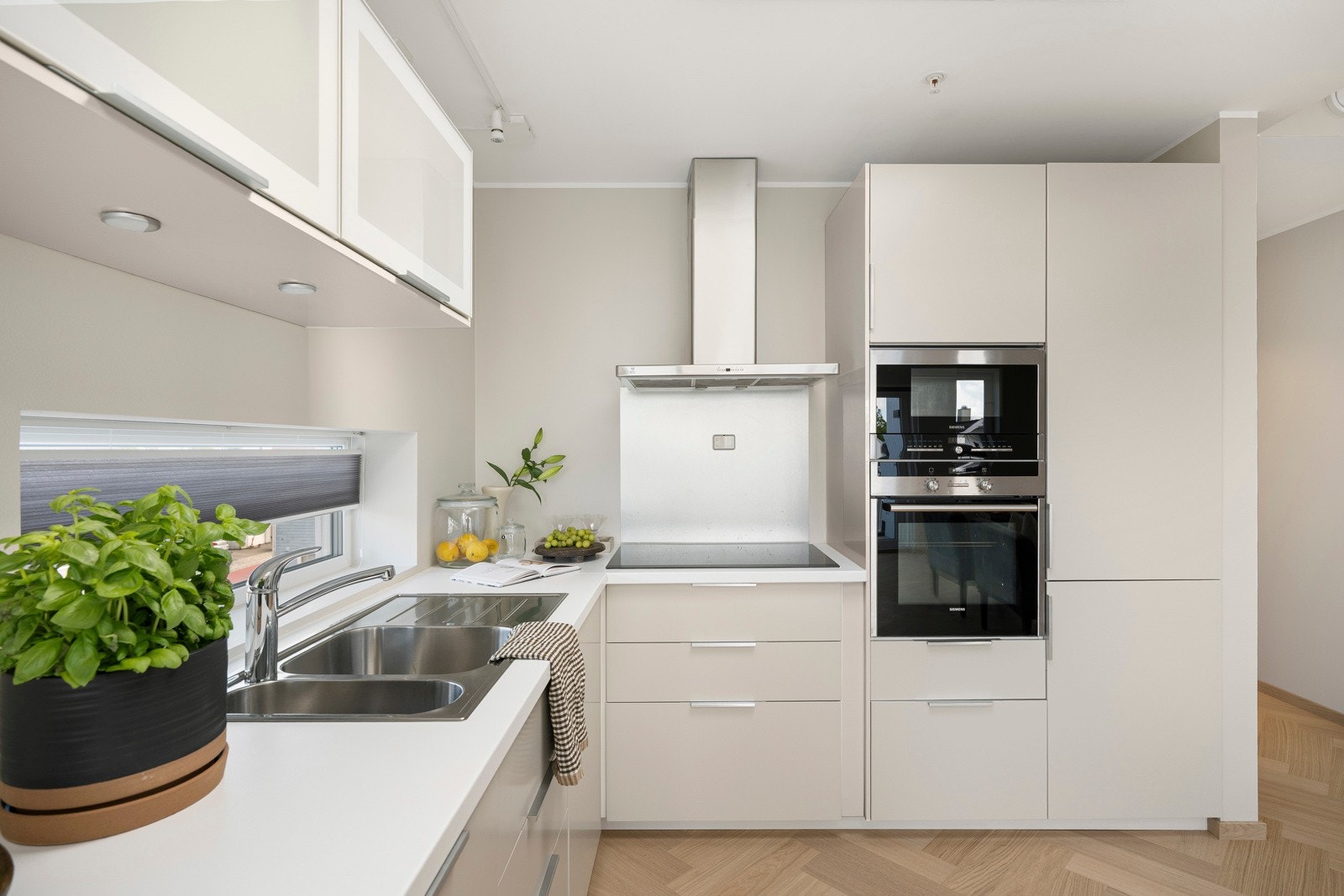 Frontene er lakkert beige av Viste Vågane, benkeplatene er i hvit laminat og det er tre overskap med hvite glassfronter. Galleribilde