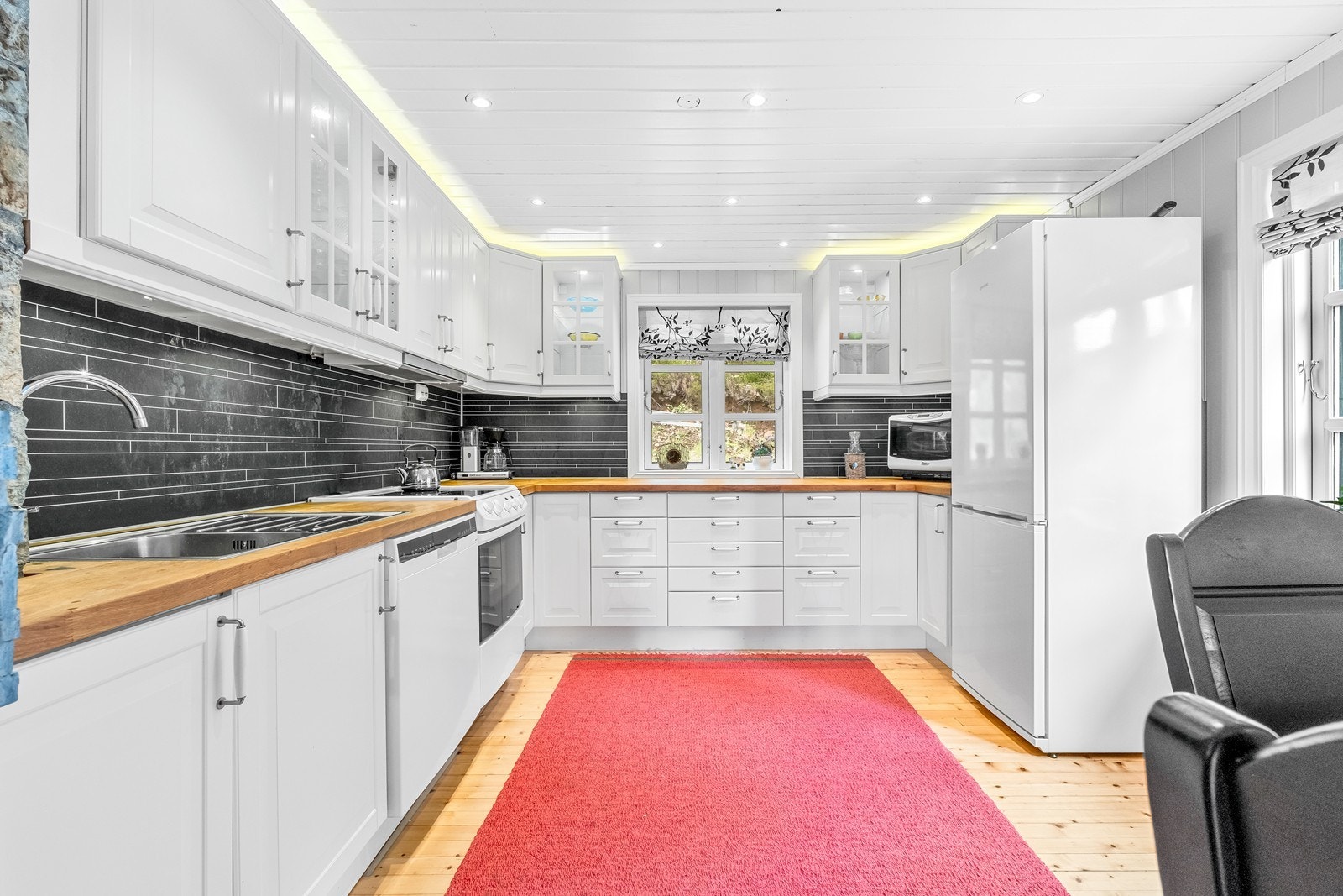 Kjøkkeninnredning med profilerte, hvite fronter og noen vitrinefronter. Galleribilde