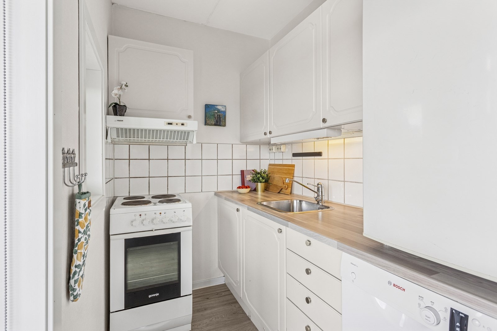 Kjøkkeninnredningen er pent utført med lyse, malte profilerte fronter og laminat benkeplate med nedfelt kjøkkenkum. Galleribilde