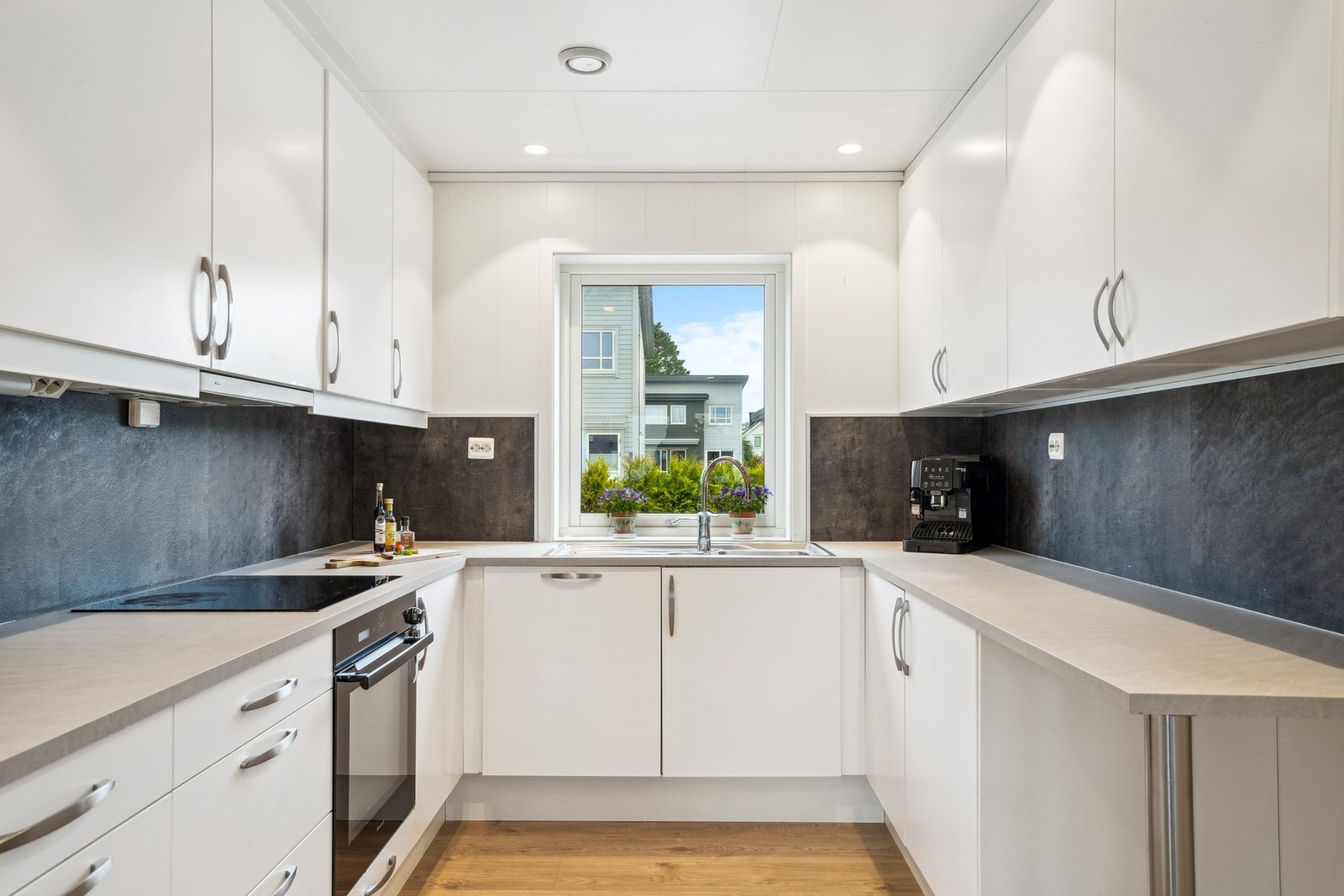 Kjøkkeninnredningen har hvite glatte fronter og en laminat benkeplate med nedfelt oppvaskkum av stål. Galleribilde