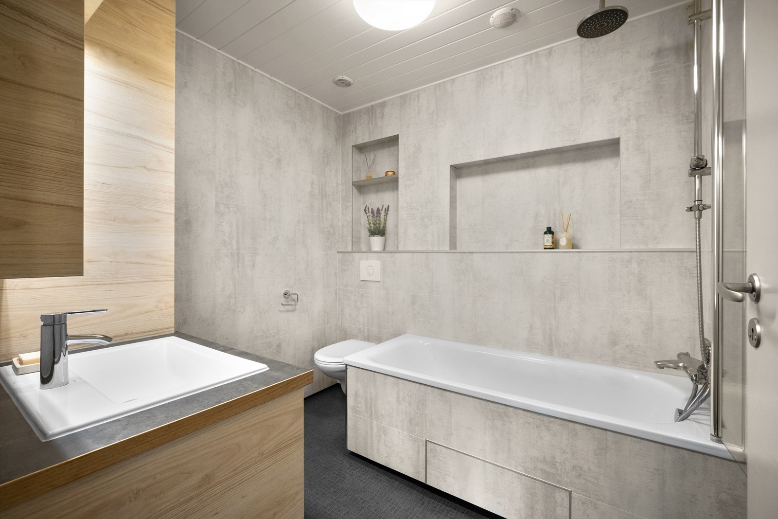 Pent bad, overflateoppusset i 2017 med moderne innredning og garnityr. Badet er innredet med veggmontert dusjvegg, badekar, veggmontert klosett, servant med skuffer og speilskap. Galleribilde
