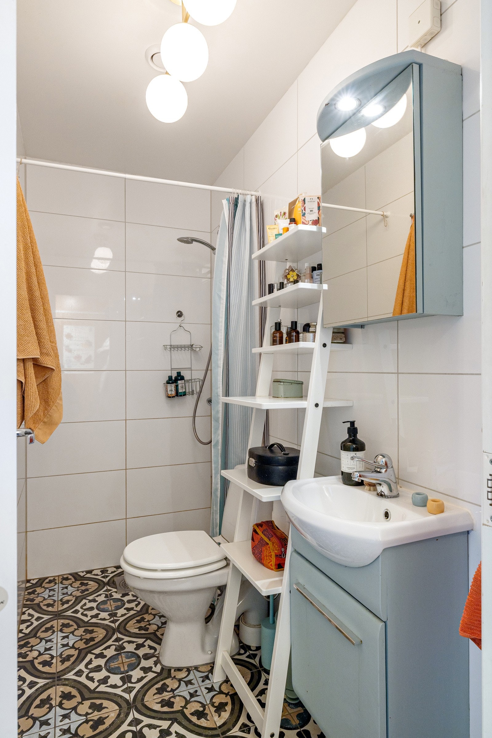 Blåmalt innredning med ovenpåliggende servant og speilskap med belysning over. Baderommet er også utstyrt med dusjhjørne med forheng og gulvstående toalett. Galleribilde