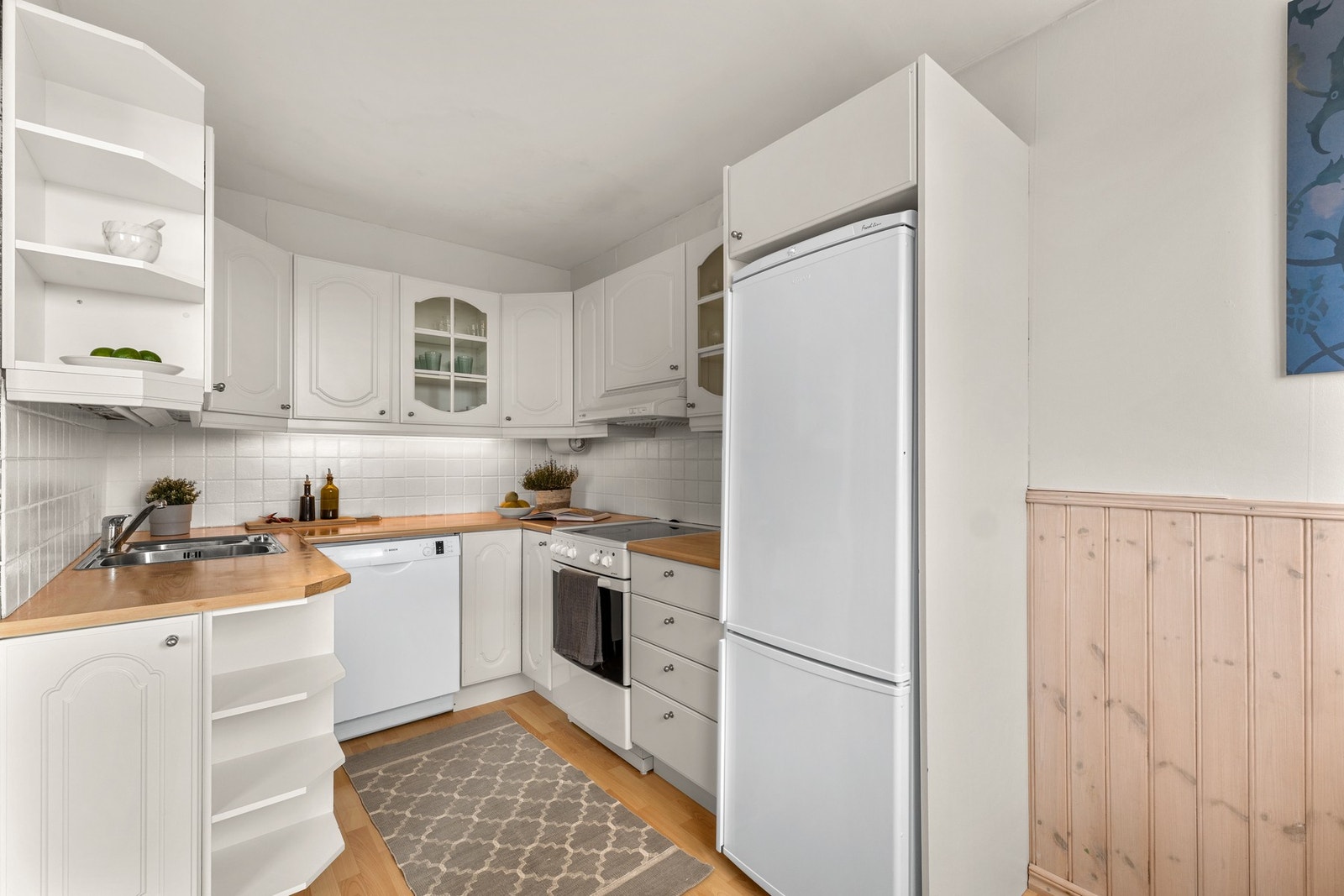 Kjøkkenet er lyst og pent med hvite profilerte fronter og enkelte vitrinedører på overskapene Galleribilde