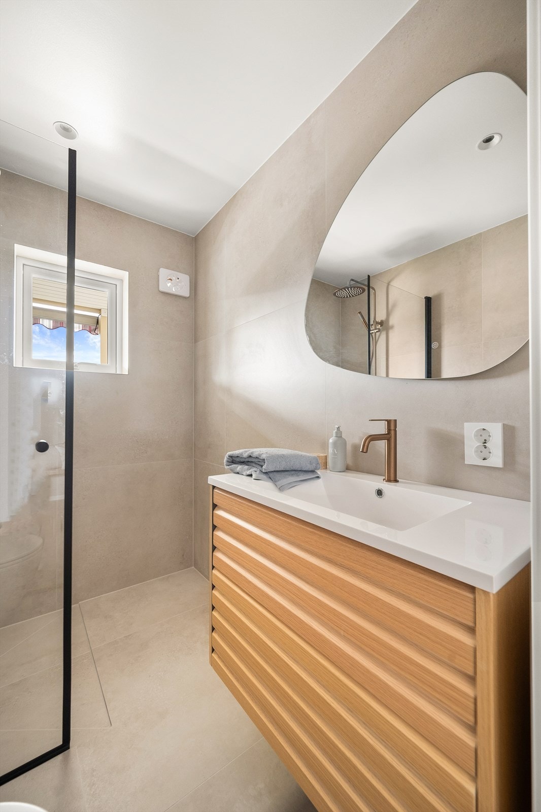 Badet er utstyrt med dusjsone med svingbar dusjvegg i glass på en side, vegghengt toalett med skjult sisterne og tidsriktig innredning med skuffer, servant med ettgreps kran og speil med innebygget lys. Galleribilde