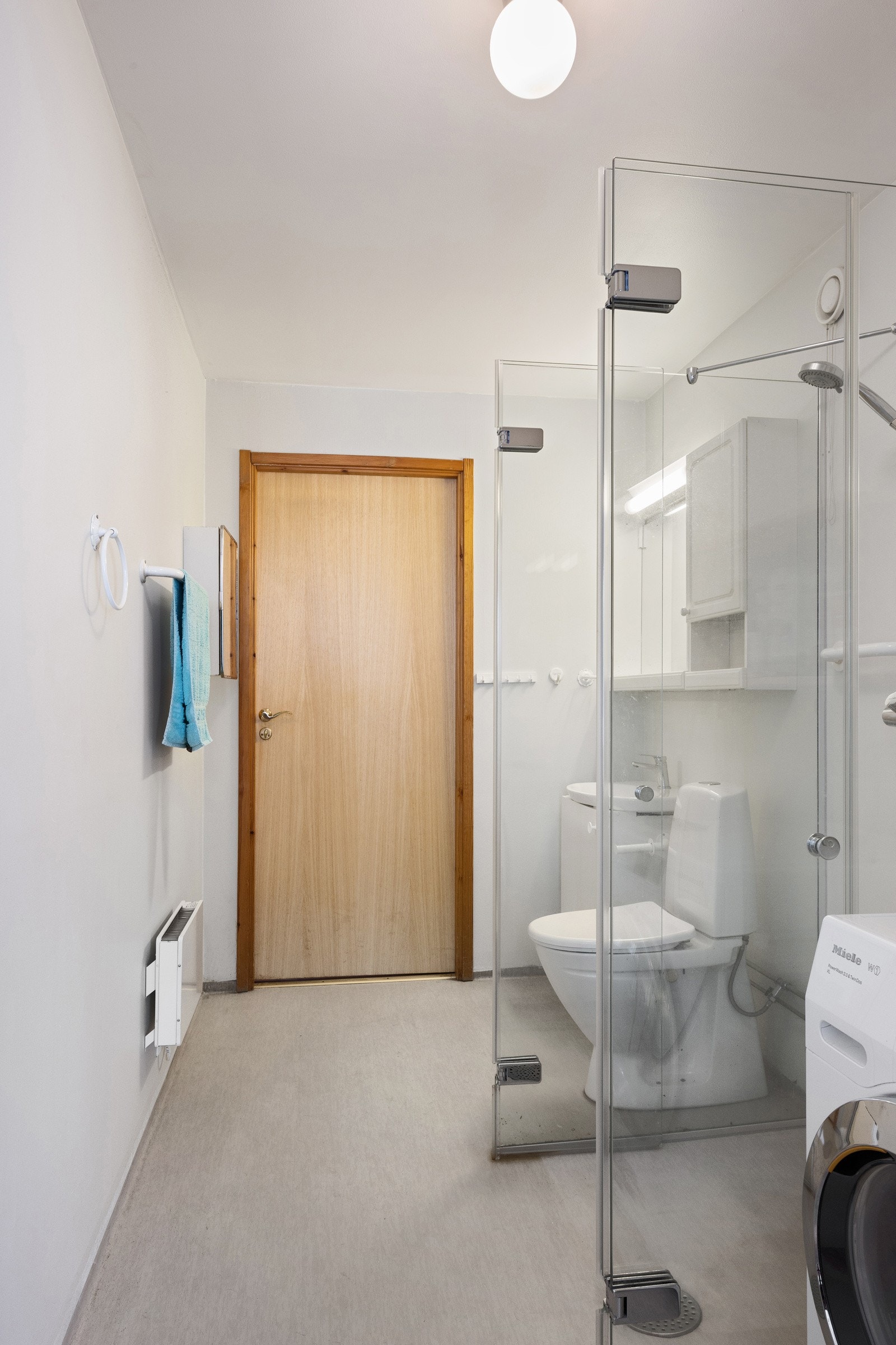 Praktisk terskelfritt baderom med dusjplass med glassdører på siden, opplegg for vaskemaskin og servant med spelskap. Galleribilde