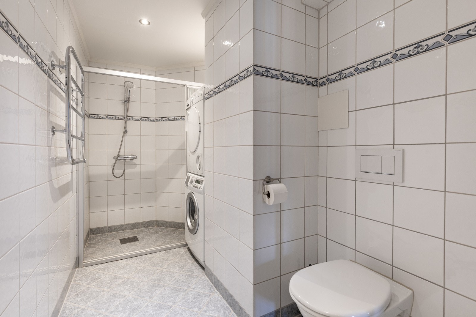 Badet har lysegrå gulvfliser med varme og hvite veggfliser med noe dekor. Galleribilde