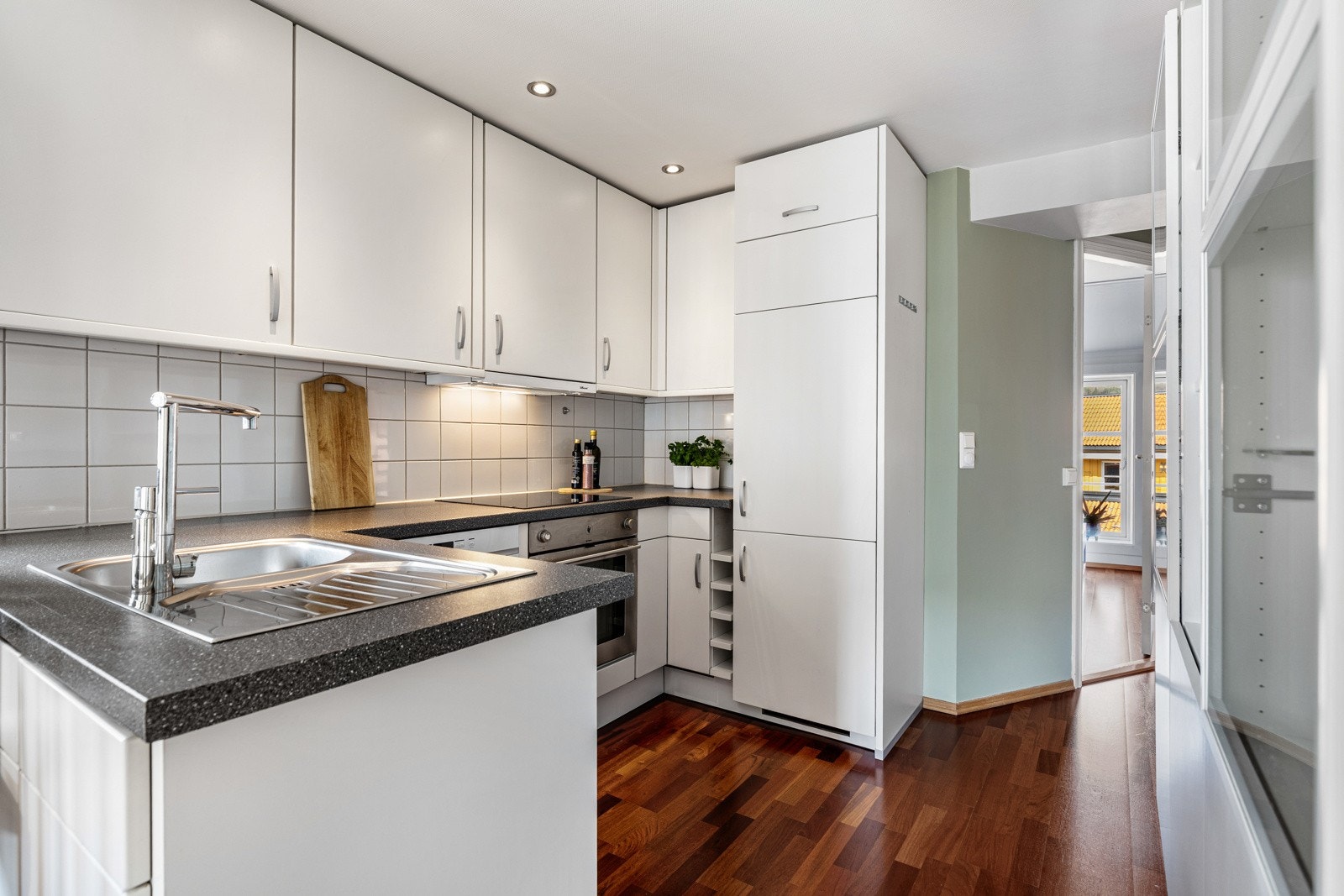 Hvite fliser er montert over benken, og over kokesonen har kjøkkenet en ventilator med belysning. Galleribilde